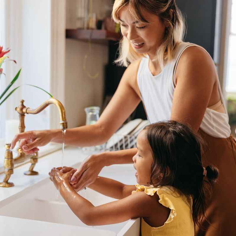 Adult and a child washing their hands in a kitchen sink